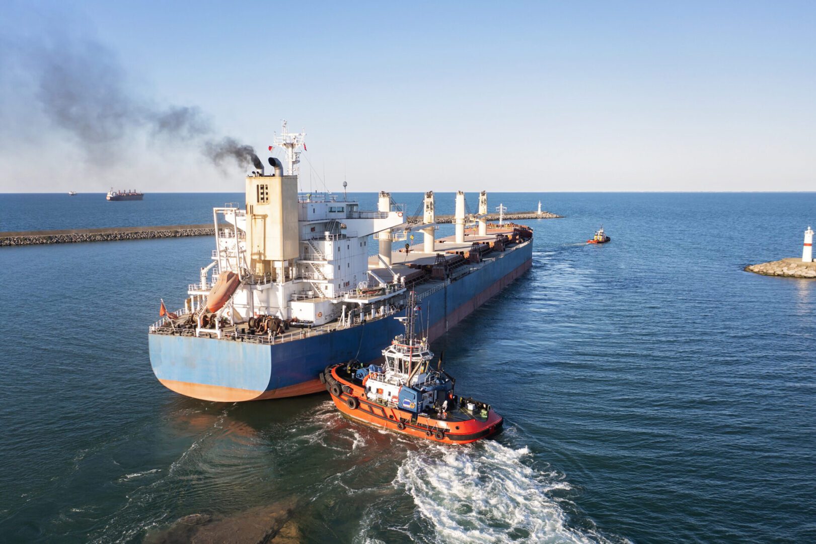Cargo ship escorted by tugboat at sea.